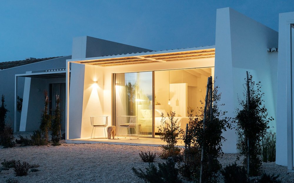 White farmhouse suite with warmly lit windows at blue hour at Amaria