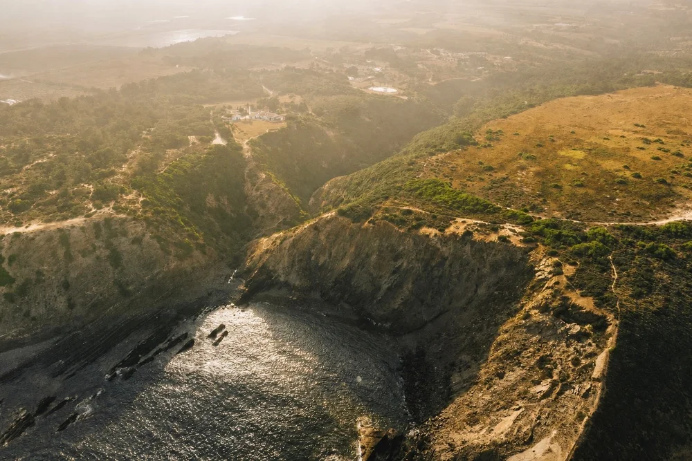 Golden aerial view of a rocky Atlantic cove with Amaria set inland on Portugal’s Costa Vicentina
