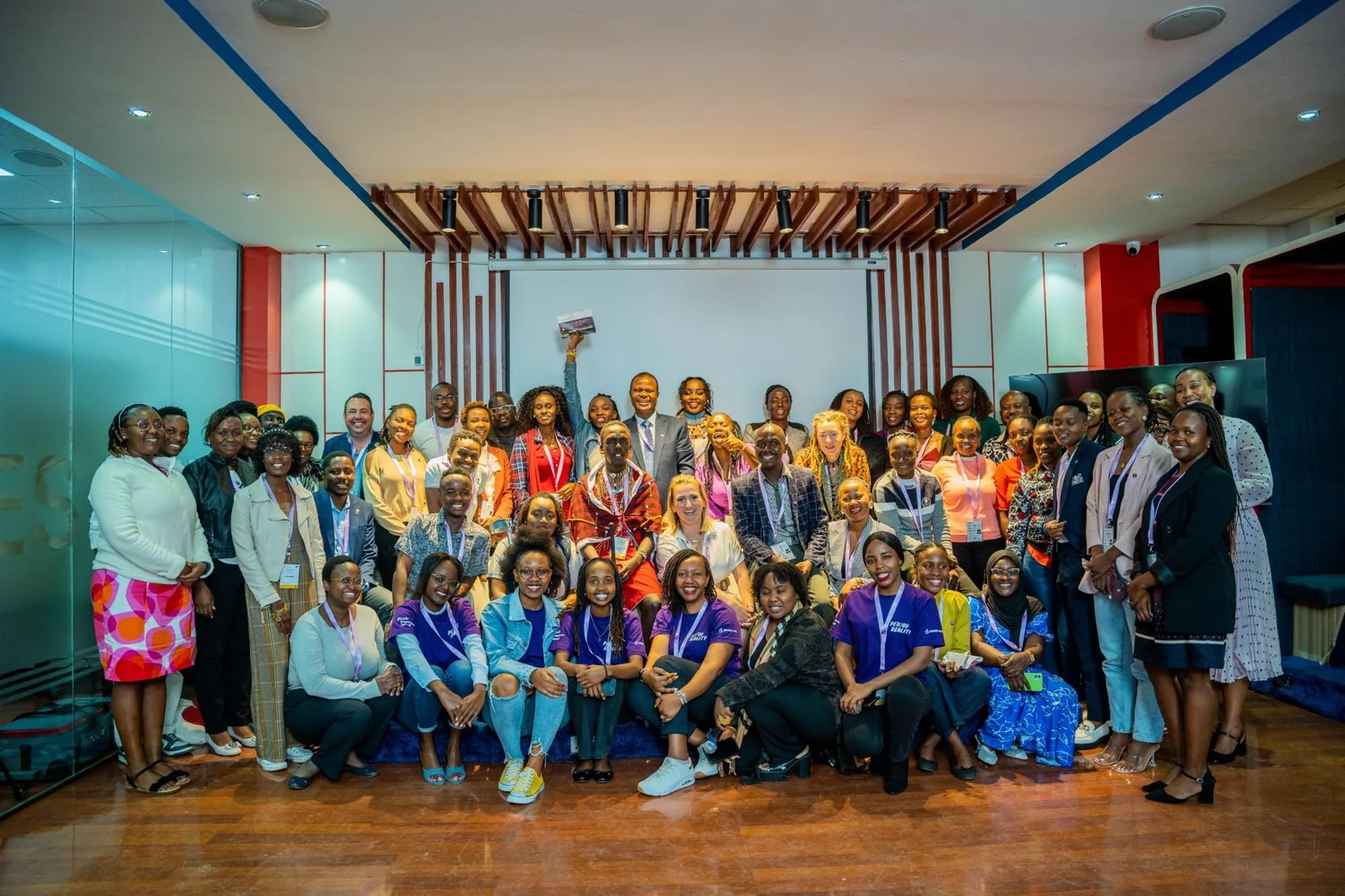 A large group of attendees, many in Period Reality T-shirts, posing together at an event