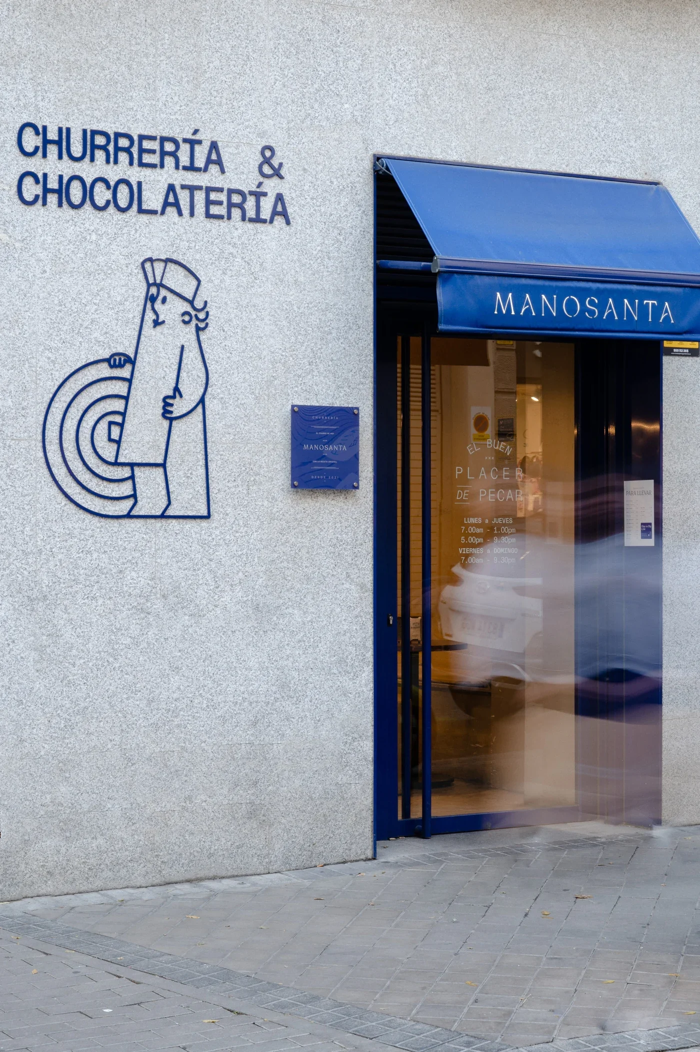 La fachada de Manosanta con su toldo azul y la ilustración del churrero