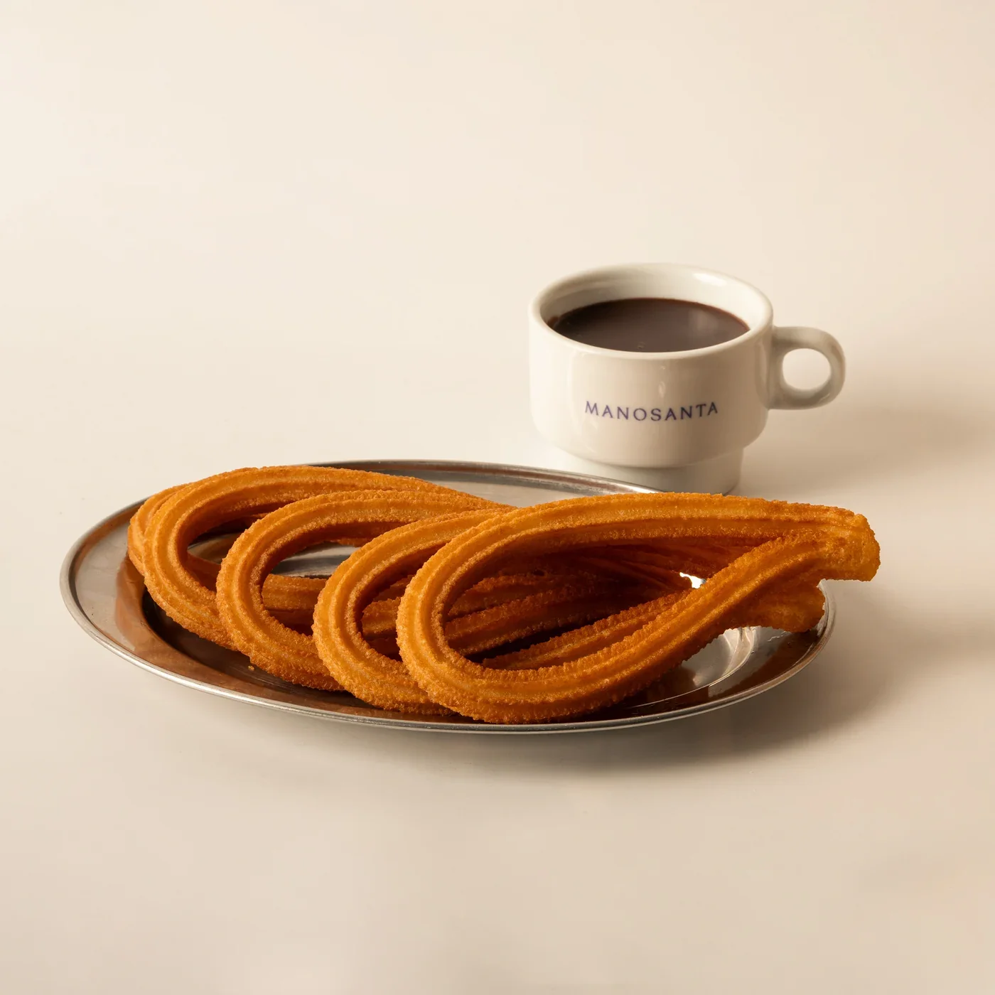 Una taza de chocolate Manosanta junto a un plato de churros