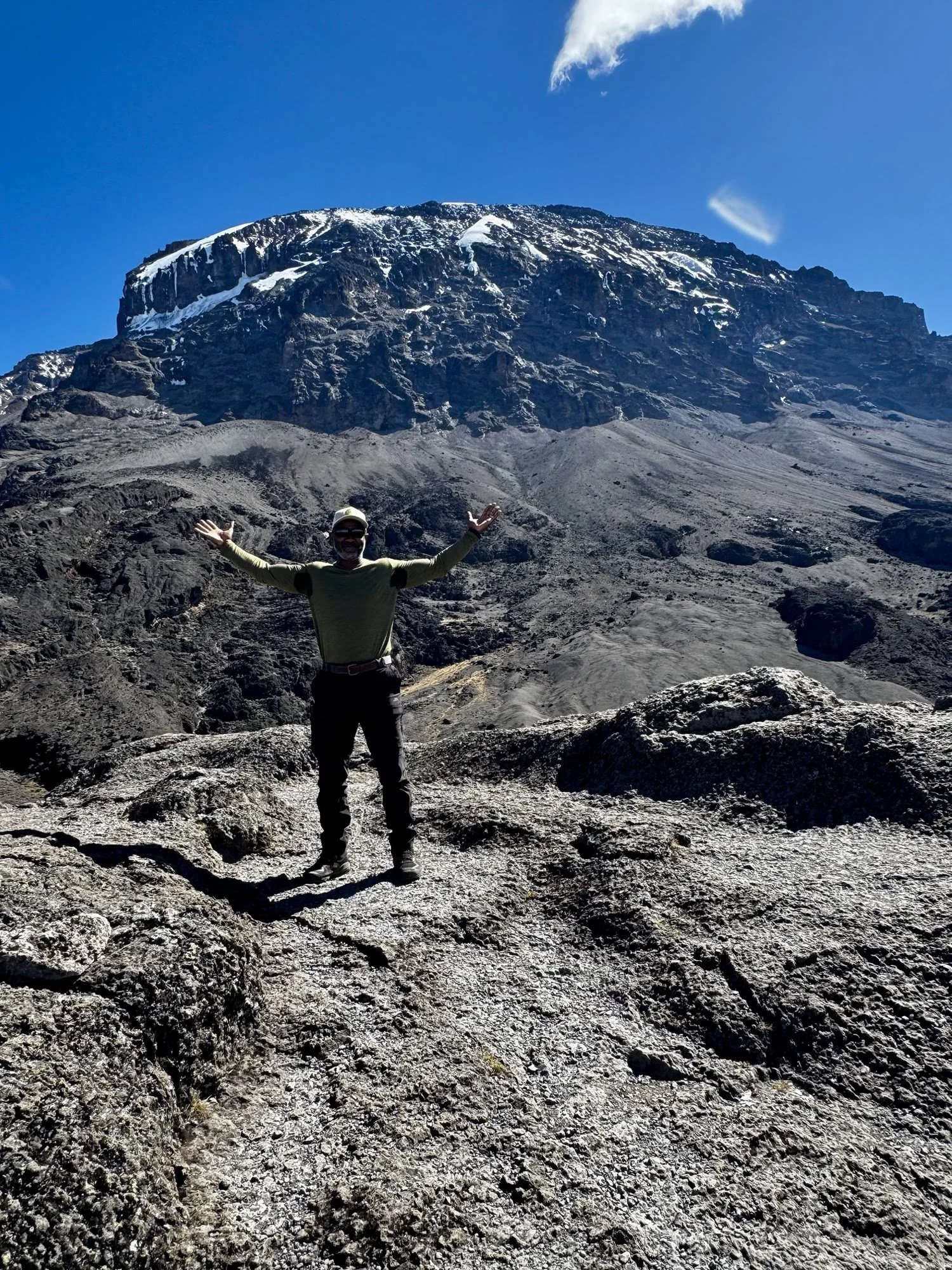 Luciano Kydd, arms out, in front of Kibo on Mount Kilimanjaro