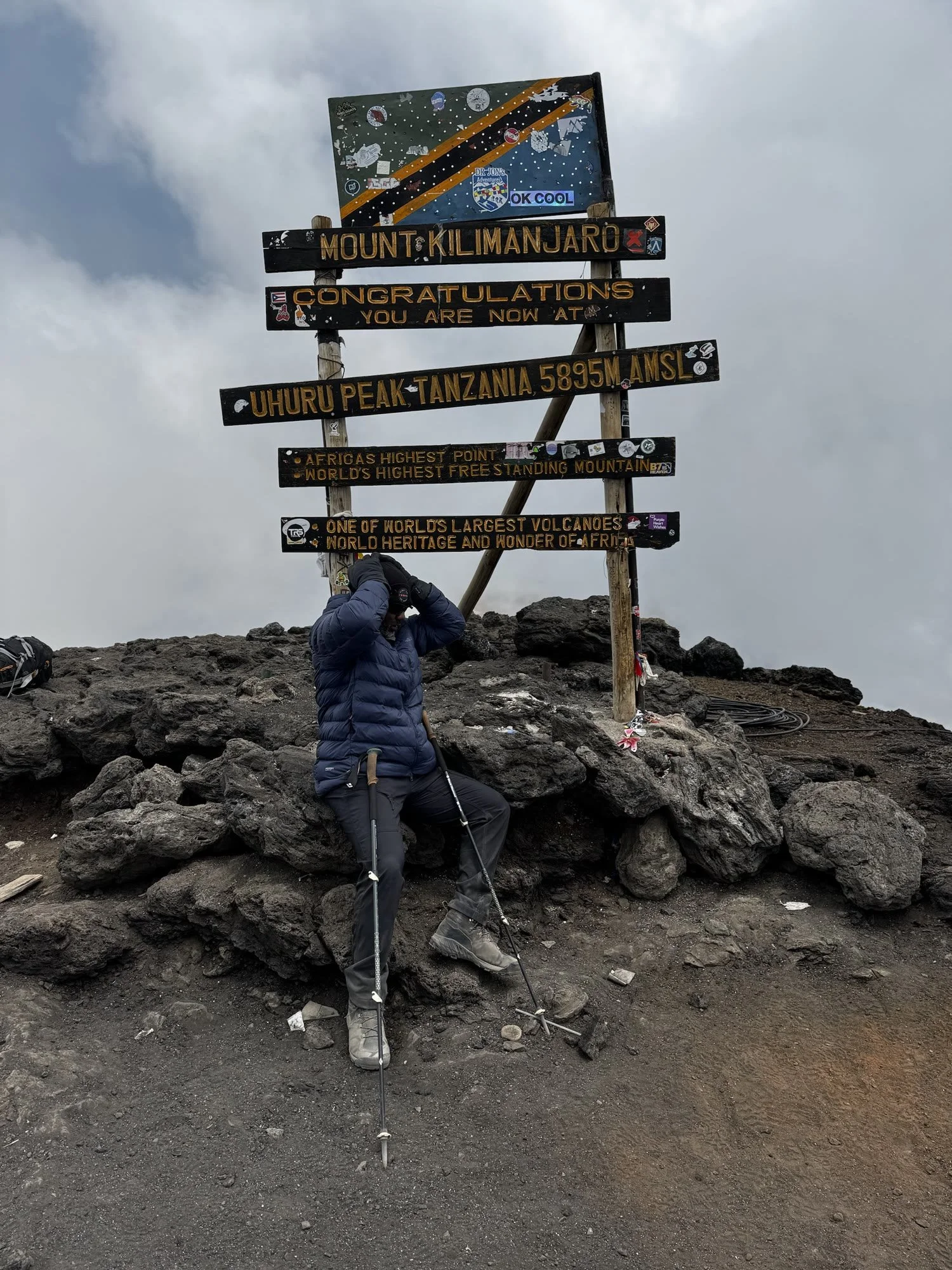 Luciano at the Uhuru Peak sign with his head in his hands