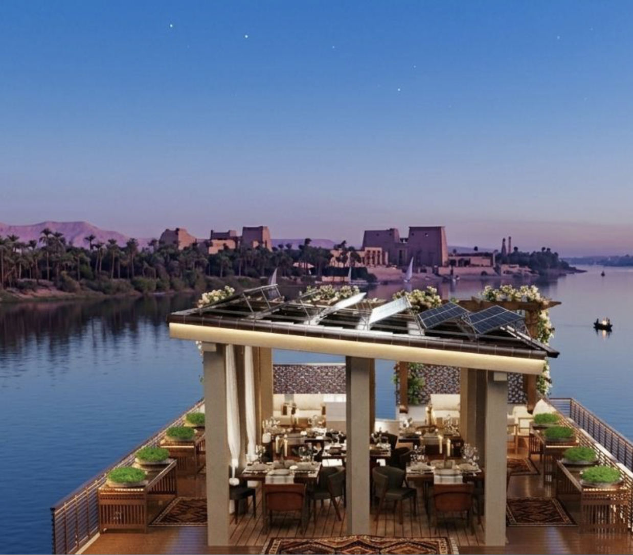 Shaded top deck dining on a Nile dahabiya with temples on the riverbank at dusk