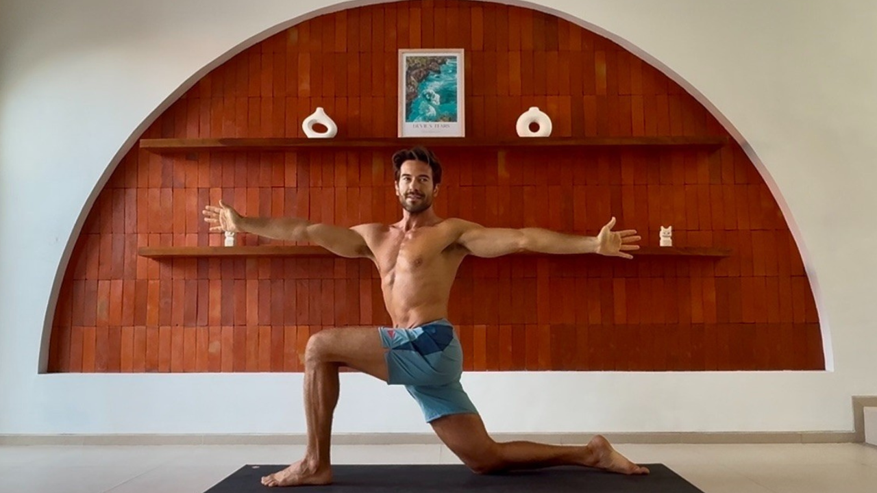 Tim smiling in a lunging warrior pose in a studio
