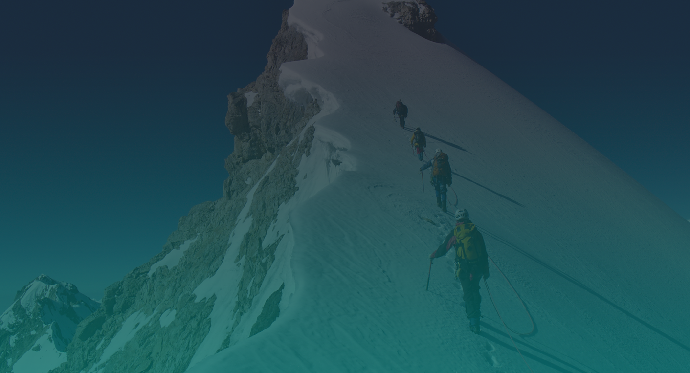 A roped team of climbers working their way up a snow ridge toward a rocky summit
