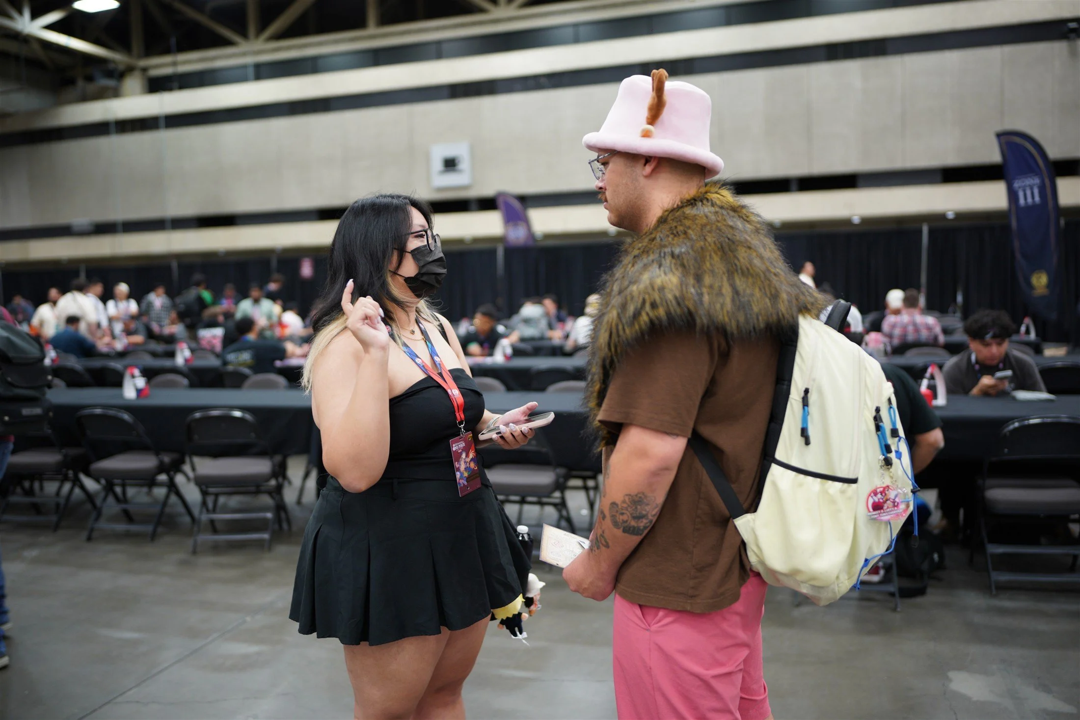 Two ONE PIECE fans, including one wearing a pink Chopper-style hat, talking beside the Dallas tournament tables