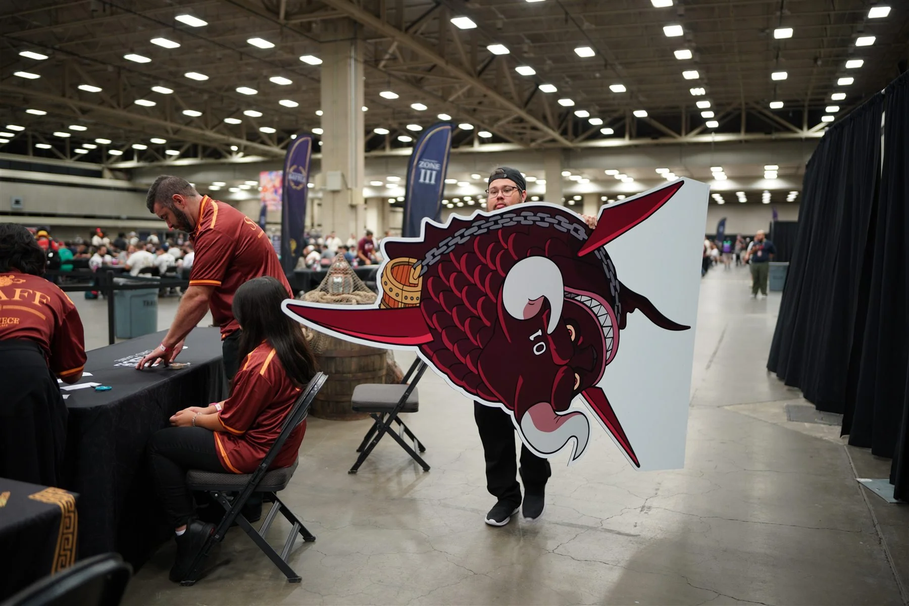 An event team member carrying a large red fish-shaped prop beside the Dallas event tables