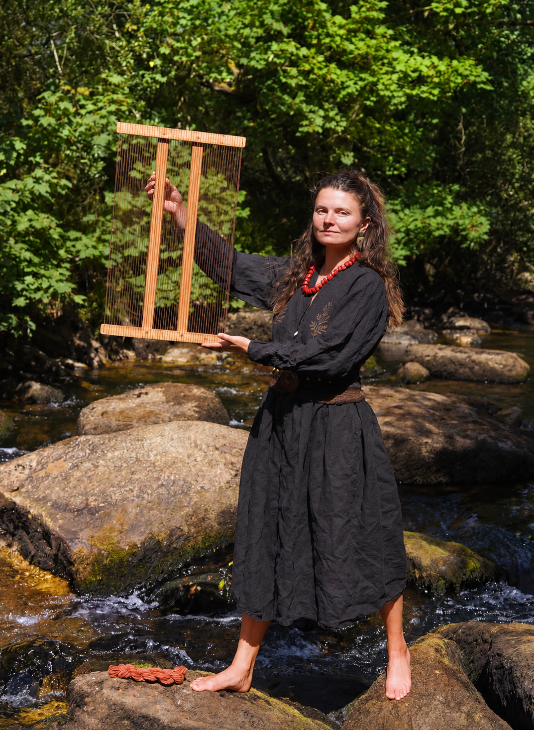 Rosemary Riedel O’Brien holding a weaving frame beside a Dartmoor stream