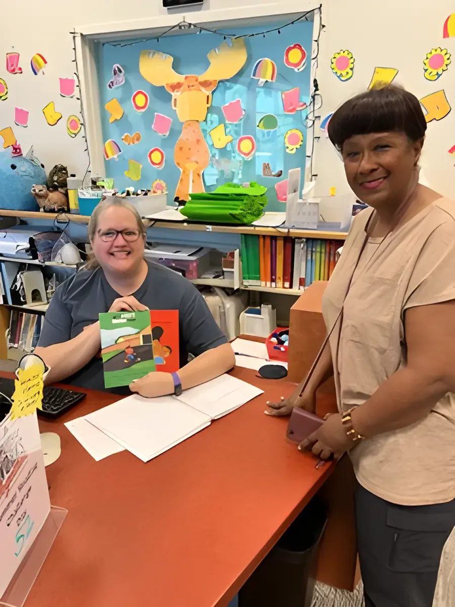 A school librarian holding a Daphne Tillman Perry book beside the author