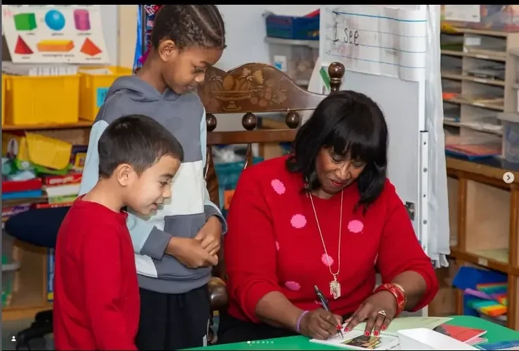 Daphne Tillman Perry signing books for two young readers in a classroom