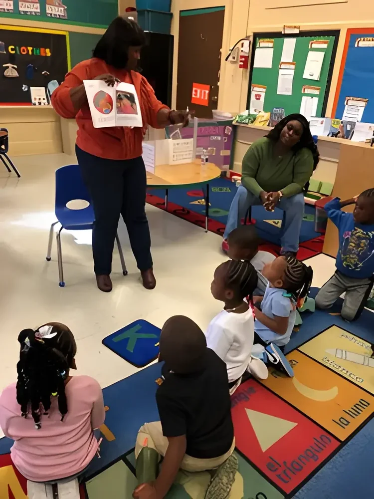 Daphne Tillman Perry showing a book illustration to children on a classroom rug