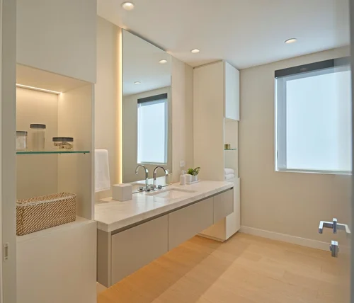 Salle de bains avec meuble vasque suspendu, plan en pierre claire, grand miroir éclairé et niche à étagère en verre
