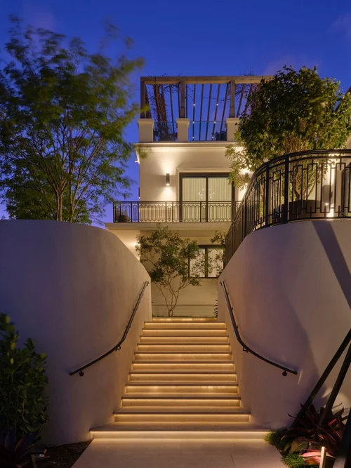Escalier extérieur éclairé entre deux murs courbes, montant vers la villa la nuit