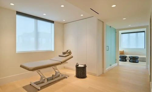 Salle de soins avec table de massage, armoires blanches toute hauteur et fenêtre avec store