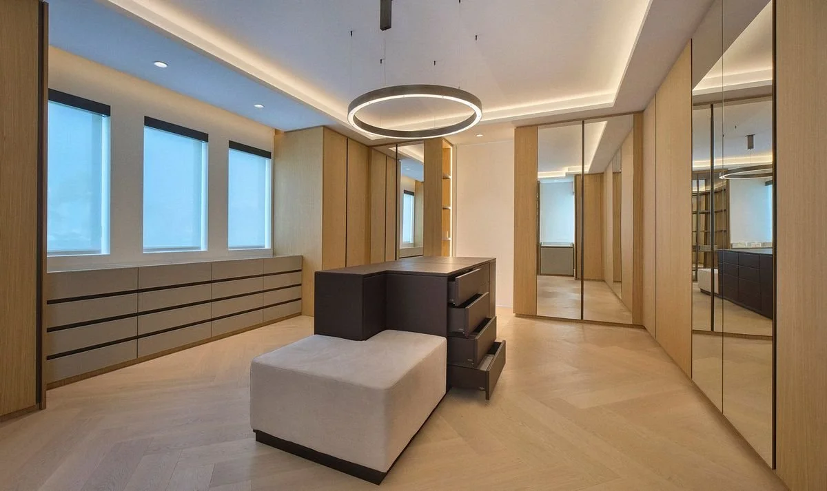Dressing avec îlot sombre à tiroirs, banquette rembourrée, suspension en anneau, armoires en bois clair et portes miroir