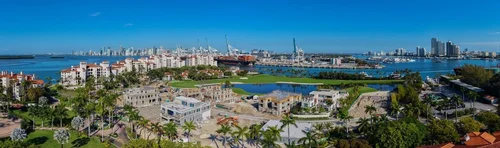 Vue aérienne panoramique de Fisher Island avec villas, palmiers, la baie, le port et la skyline de Miami à l’horizon