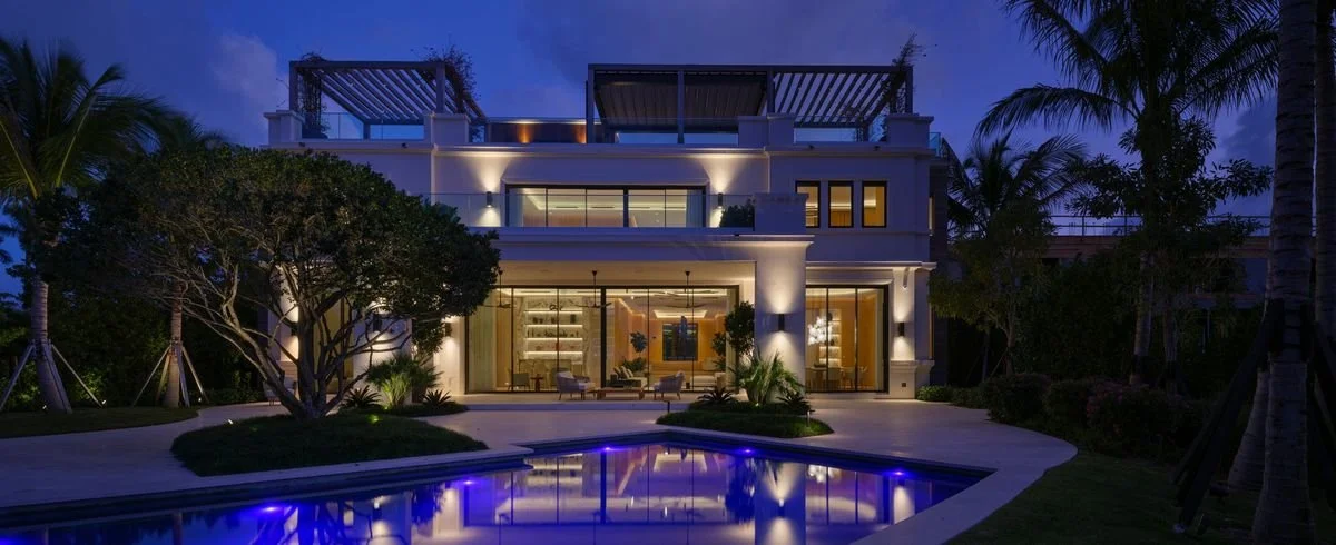 Villa la nuit avec piscine éclairée en bleu, jardin, palmiers et façade illuminée