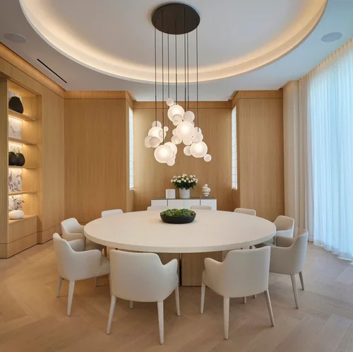 Salle à manger avec table ronde et chaises rembourrées, boiserie, niches éclairées, enfilade blanche et lustre à globes