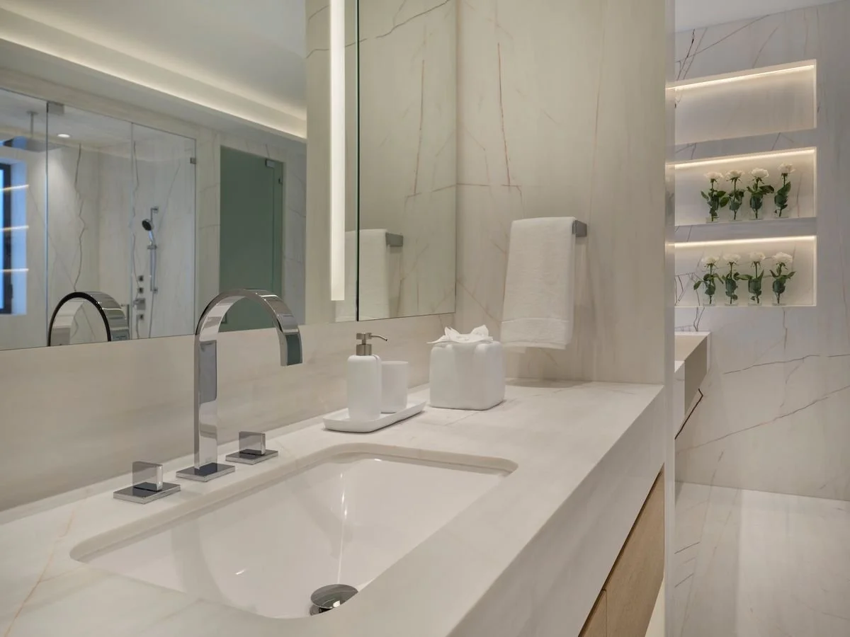 Plan en pierre claire avec vasque sous plan et robinet chromé, miroir à lumière intégrée et niches éclairées dans le mur