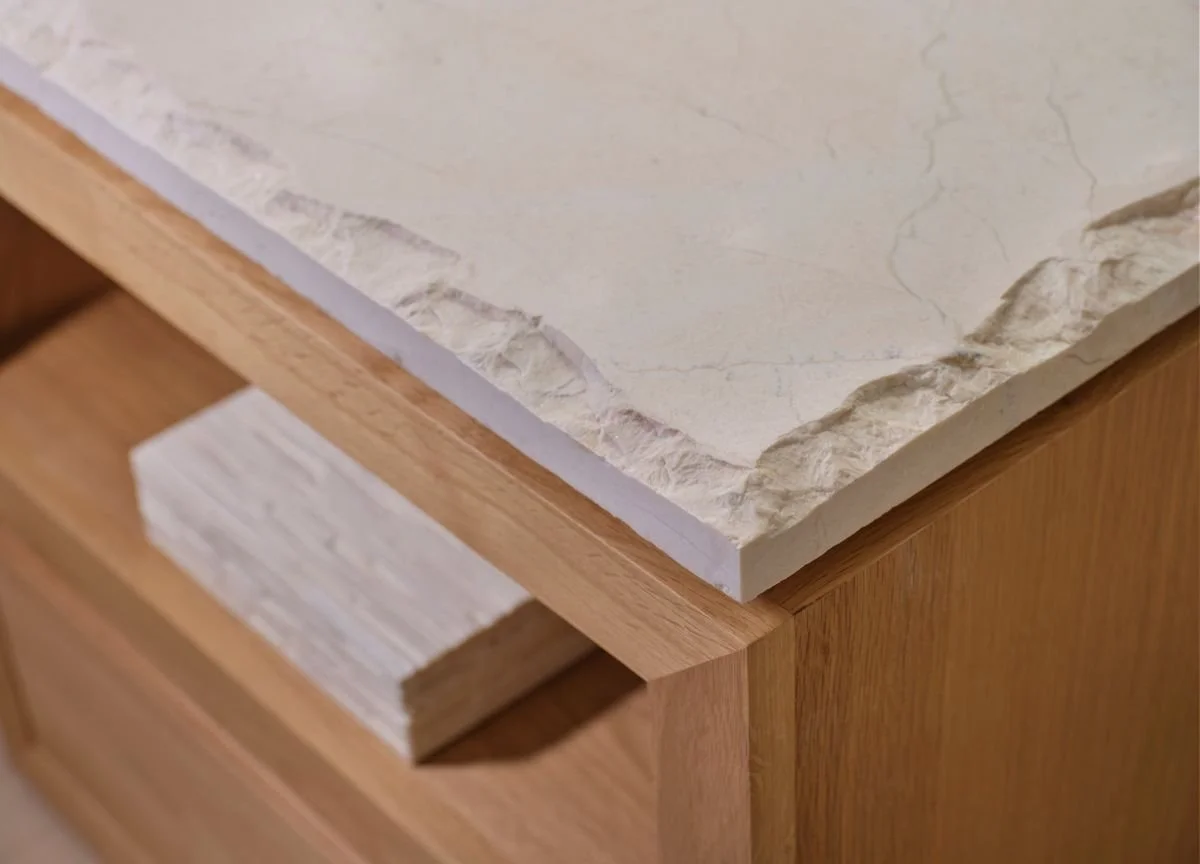 Détail d’un plateau en pierre claire au bord brut posé sur un meuble en bois