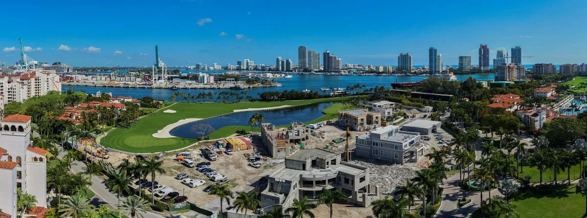 Vue aérienne de Fisher Island avec le golf, des villas parmi les palmiers, la baie et la skyline de Miami à l’horizon
