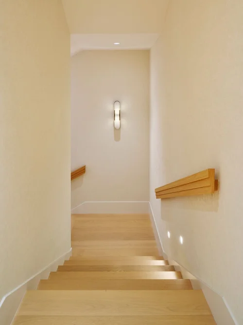 Escalier aux marches en bois clair, main courante en bois et applique murale