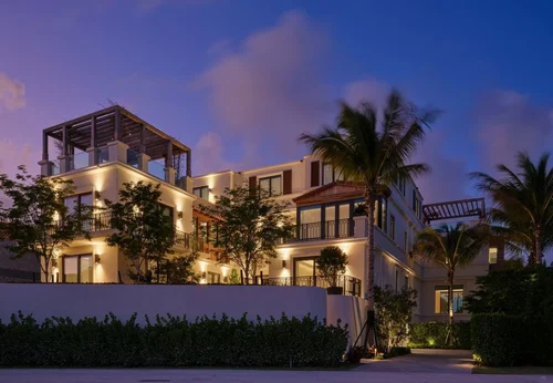 Façade de la villa au crépuscule avec lumières chaudes, terrasses, pergolas et palmiers