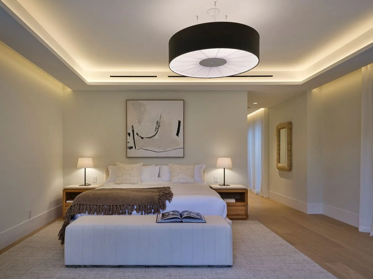 Chambre avec lit double, banquette rembourrée, suspension noire, tableau abstrait et tables de chevet en bois