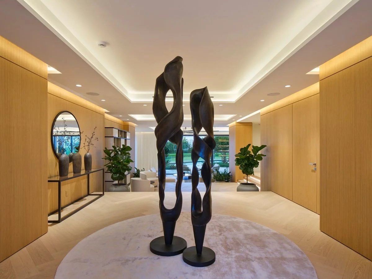 Axe de l’entrée avec boiserie de part et d’autre, console avec miroir rond, plafond à éclairage indirect et jardin au fond