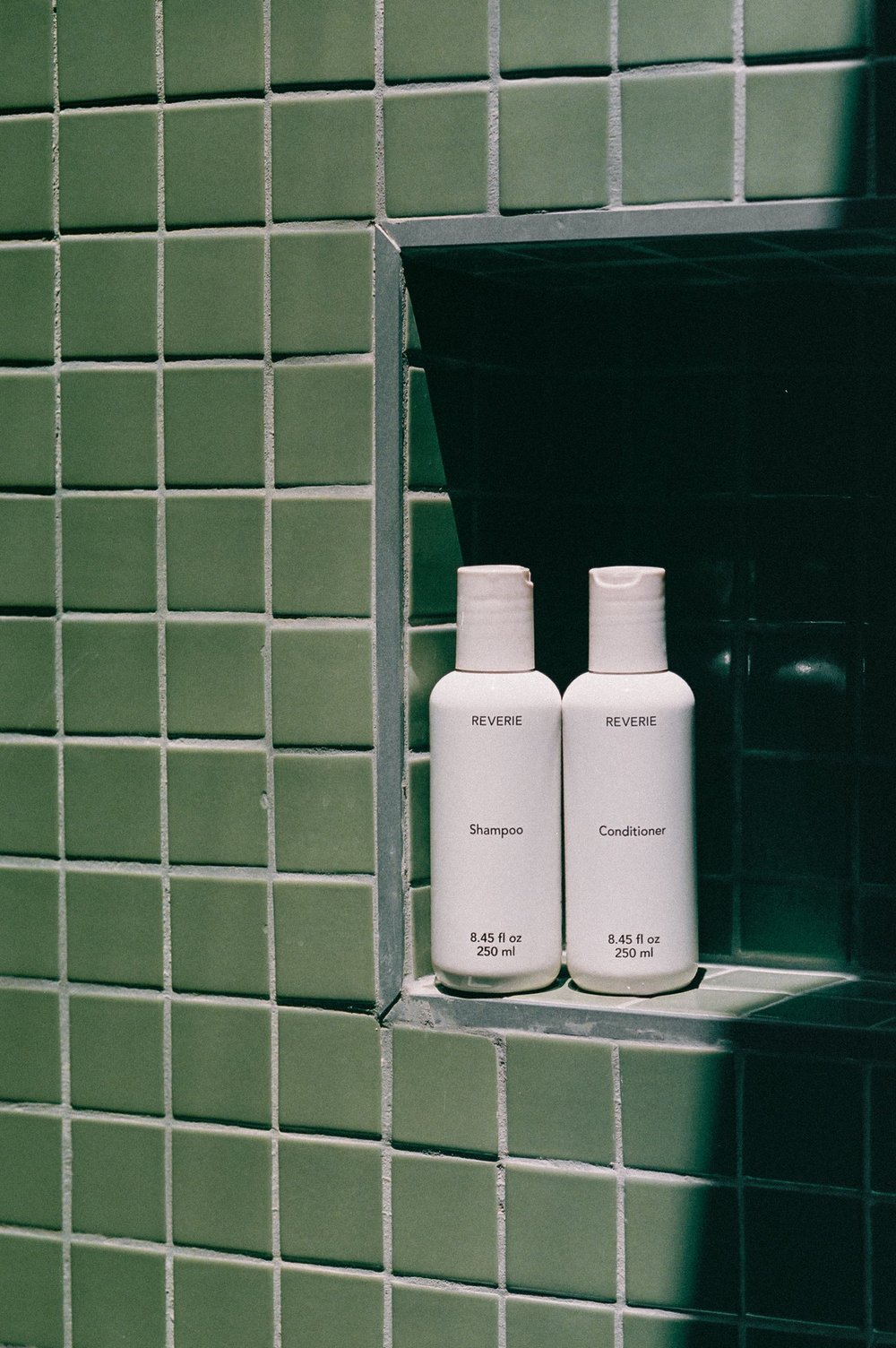 Reverie shampoo and conditioner bottles on a green tiled shelf
