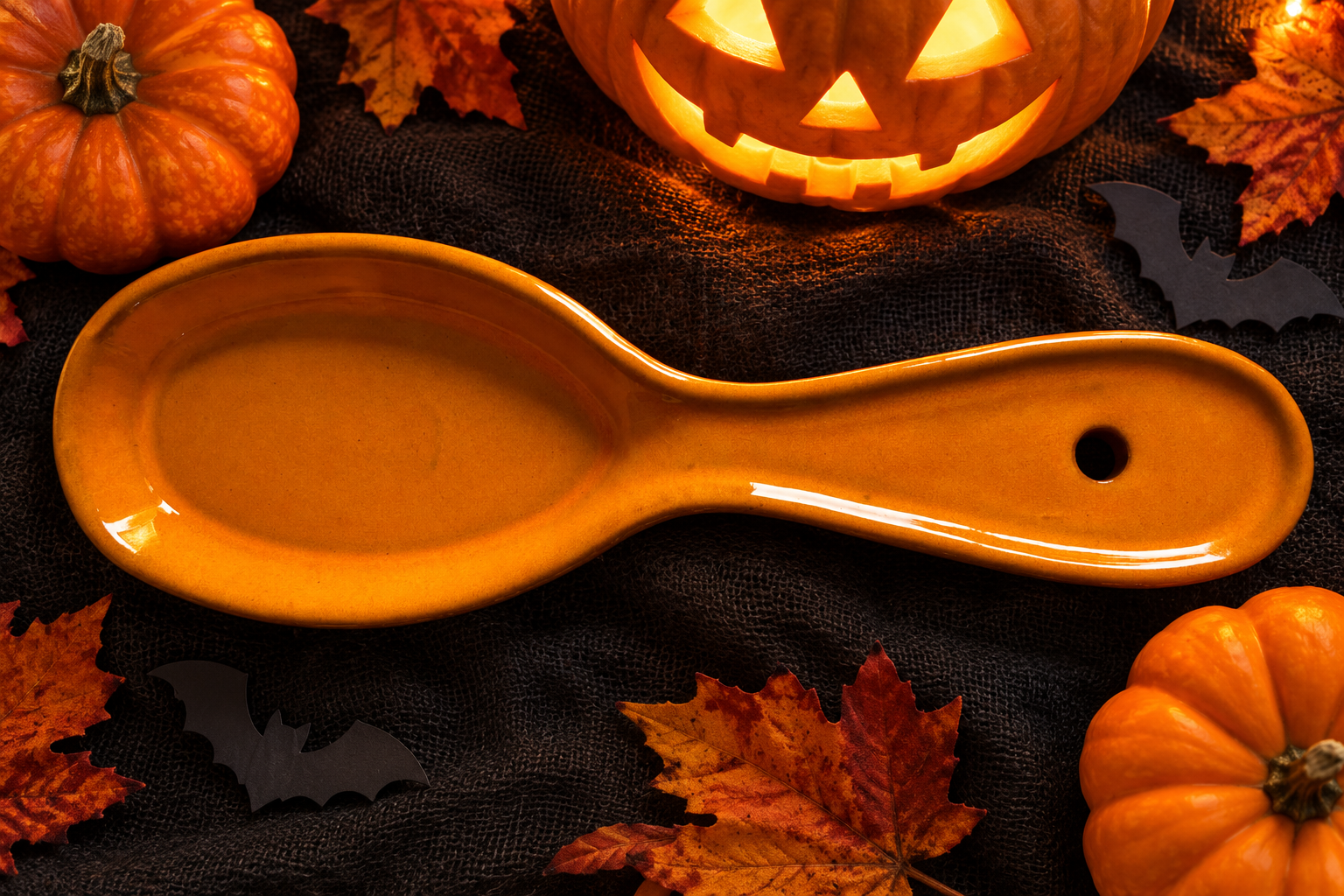 Orange spoon rest on a Halloween table with pumpkins and paper bats