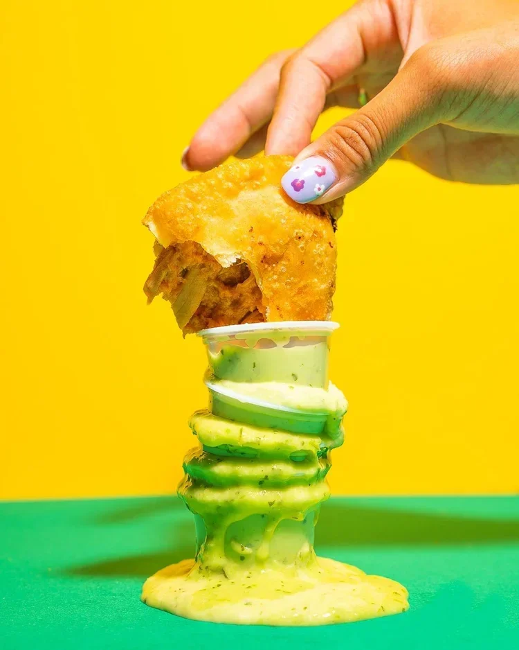 Hand dipping an empanada into green salsa