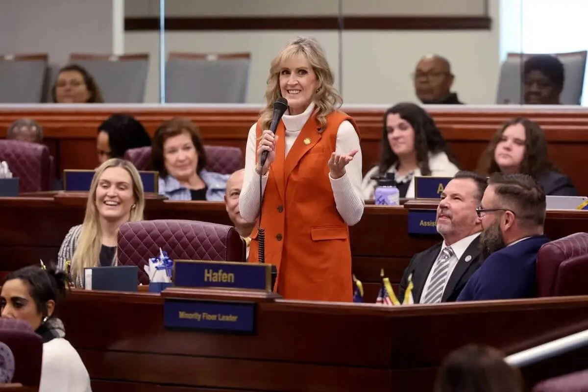 Melissa Hardy speaking into a microphone on the Nevada Assembly floor as colleagues look on