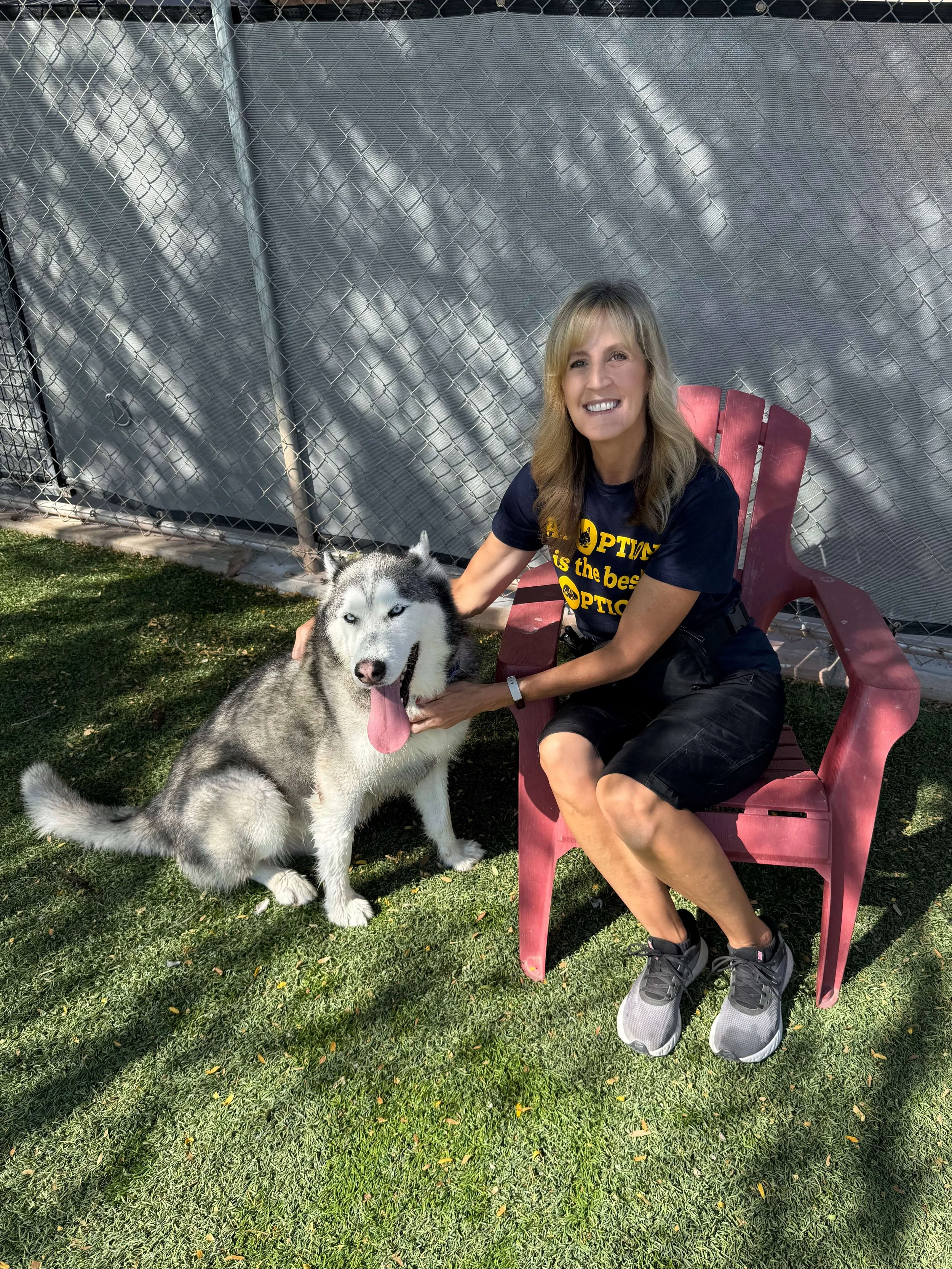 Melissa Hardy petting a husky at an animal shelter, wearing a shirt that reads Adoption is the best option