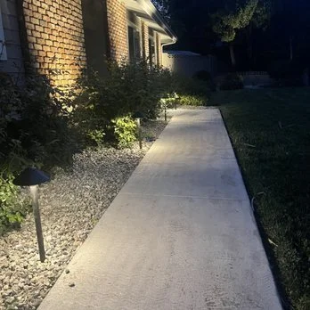 Pathway lighting installation — bollard path lights with uplighted shrubs along residential walkway