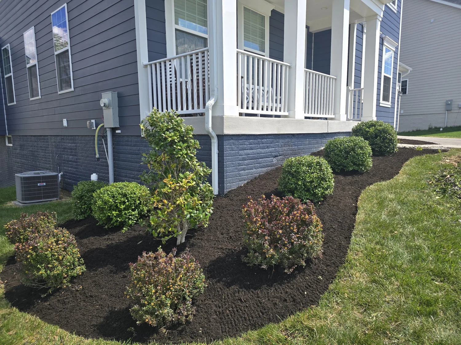 Fresh mulch and neatly trimmed shrubs beside a front porch