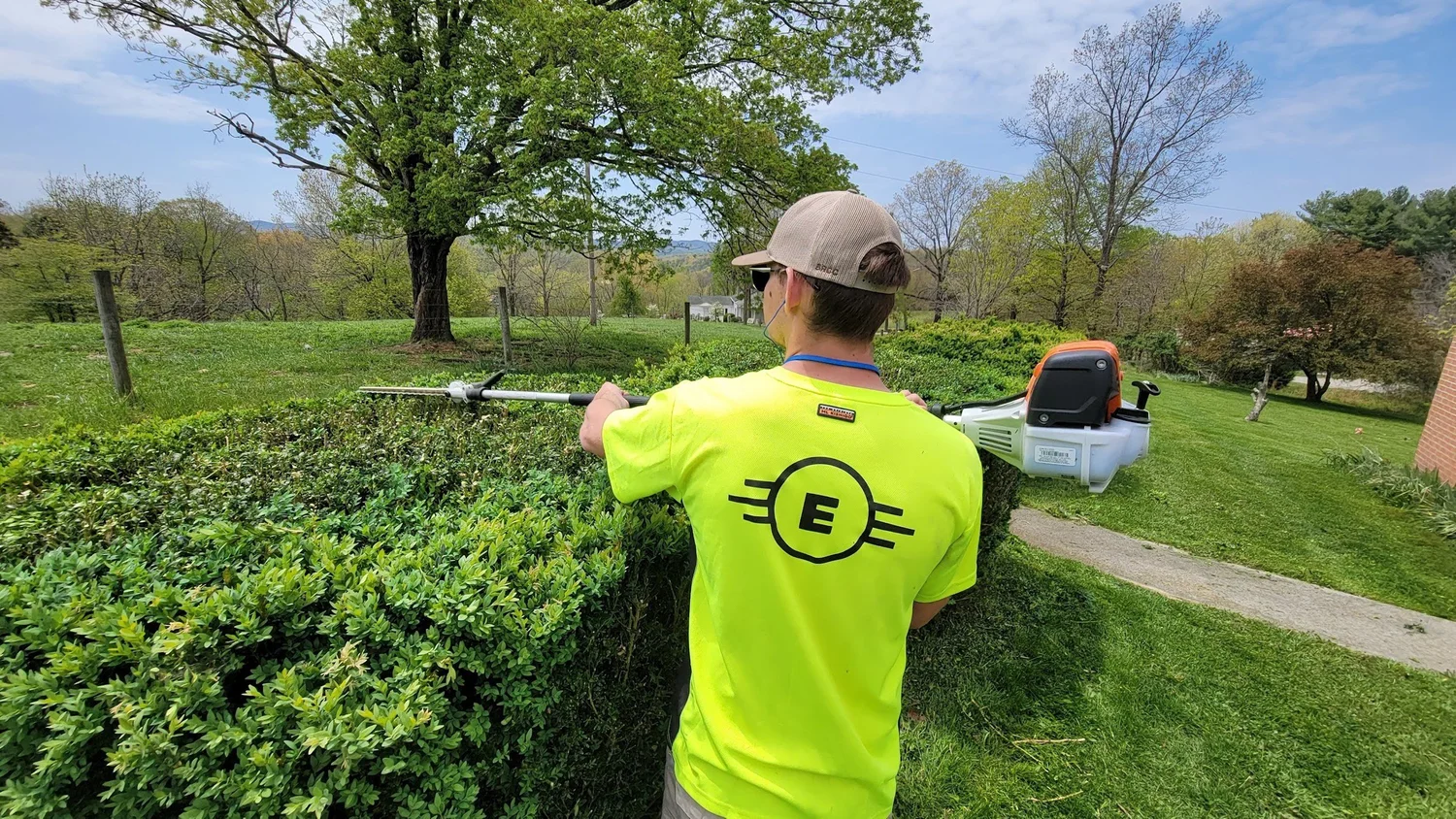 East Coast Lawns crew member trimming a hedge in a branded shirt