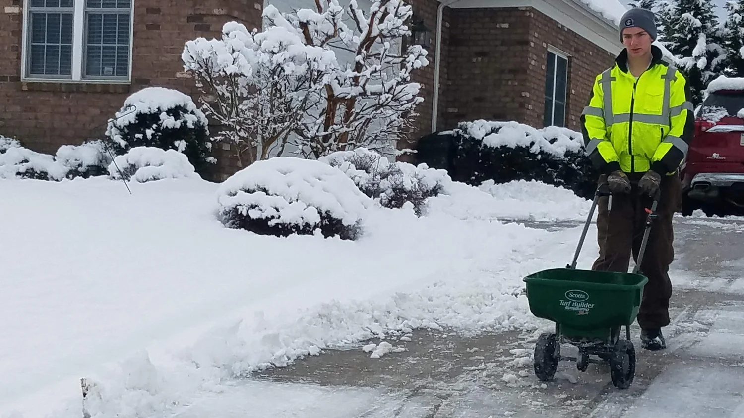 Crew member spreading deicer on a cleared walkway beside snowy landscaping