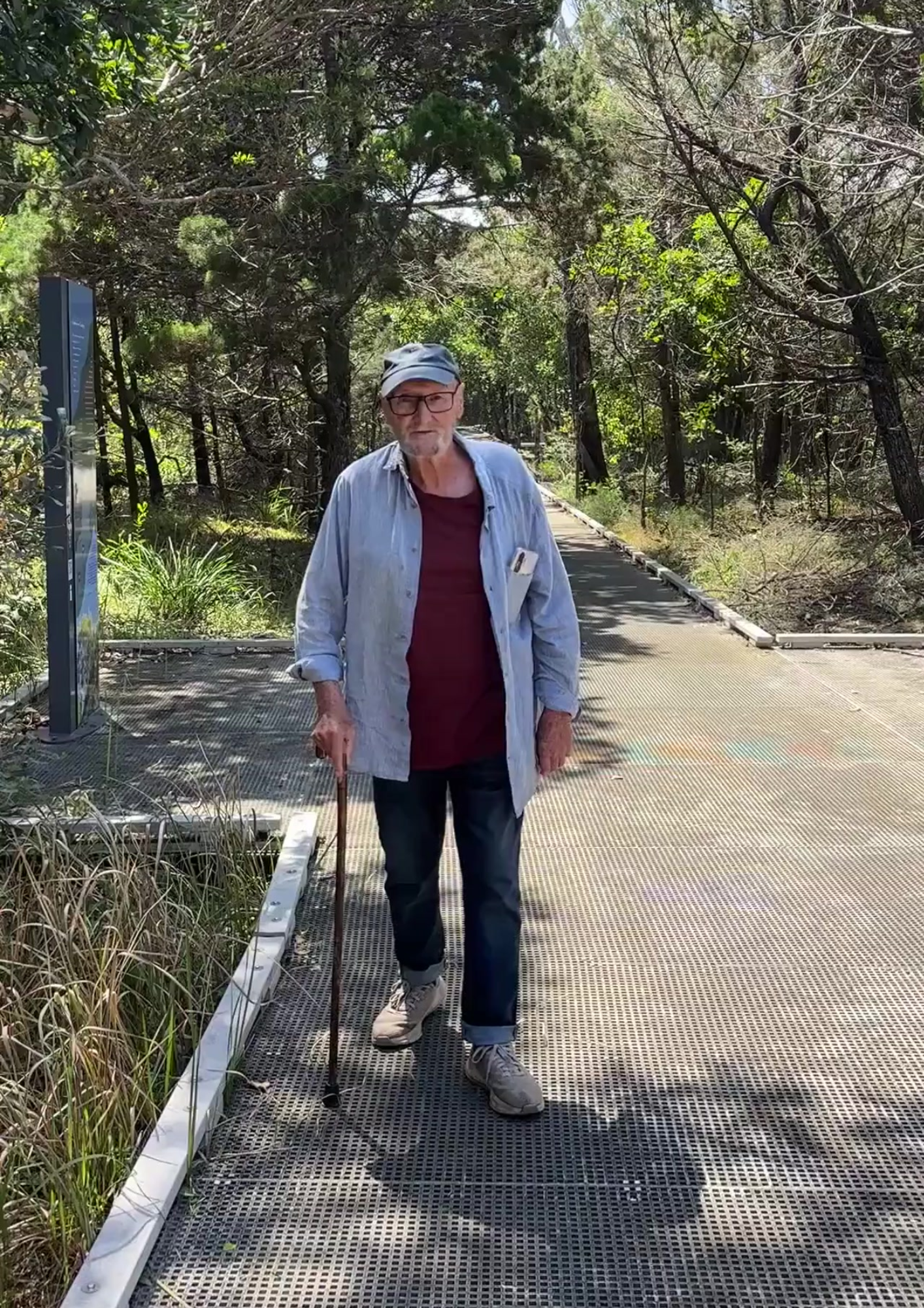 A smiling older man in a cap, chatting on a bush boardwalk