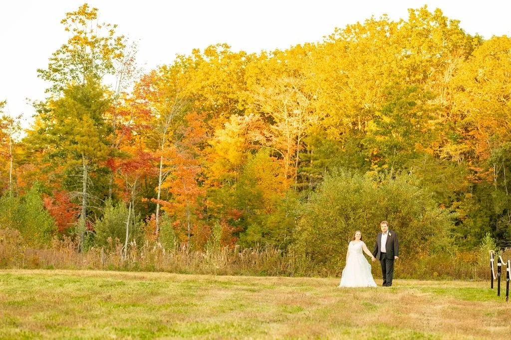 A couple walking through a golden fall field at William Allen Farm