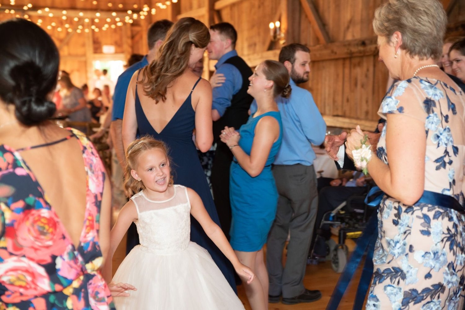 A flower girl in a white dress dancing with guests inside the barn