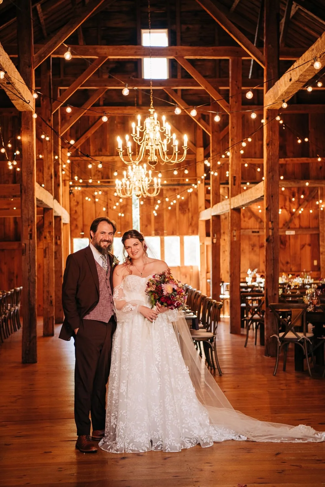 A smiling bride and groom with chandeliers and string lights behind them