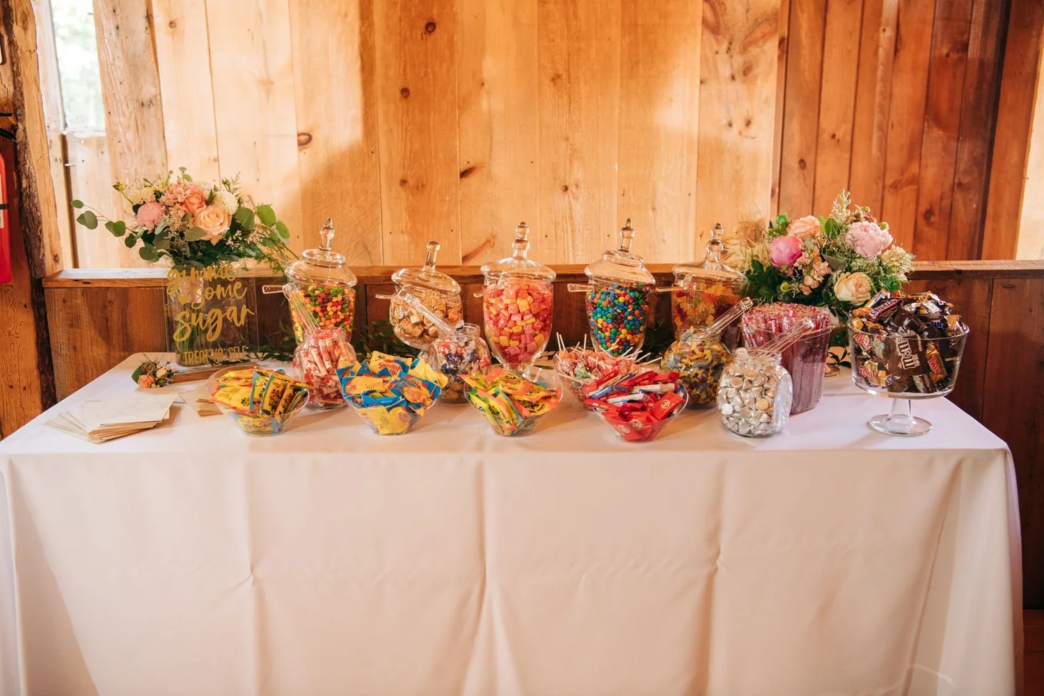 A candy bar with glass jars and fresh flowers inside the barn