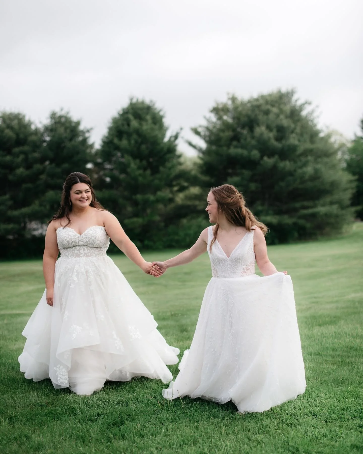Two brides holding hands and smiling as they walk across the lawn at William Allen Farm