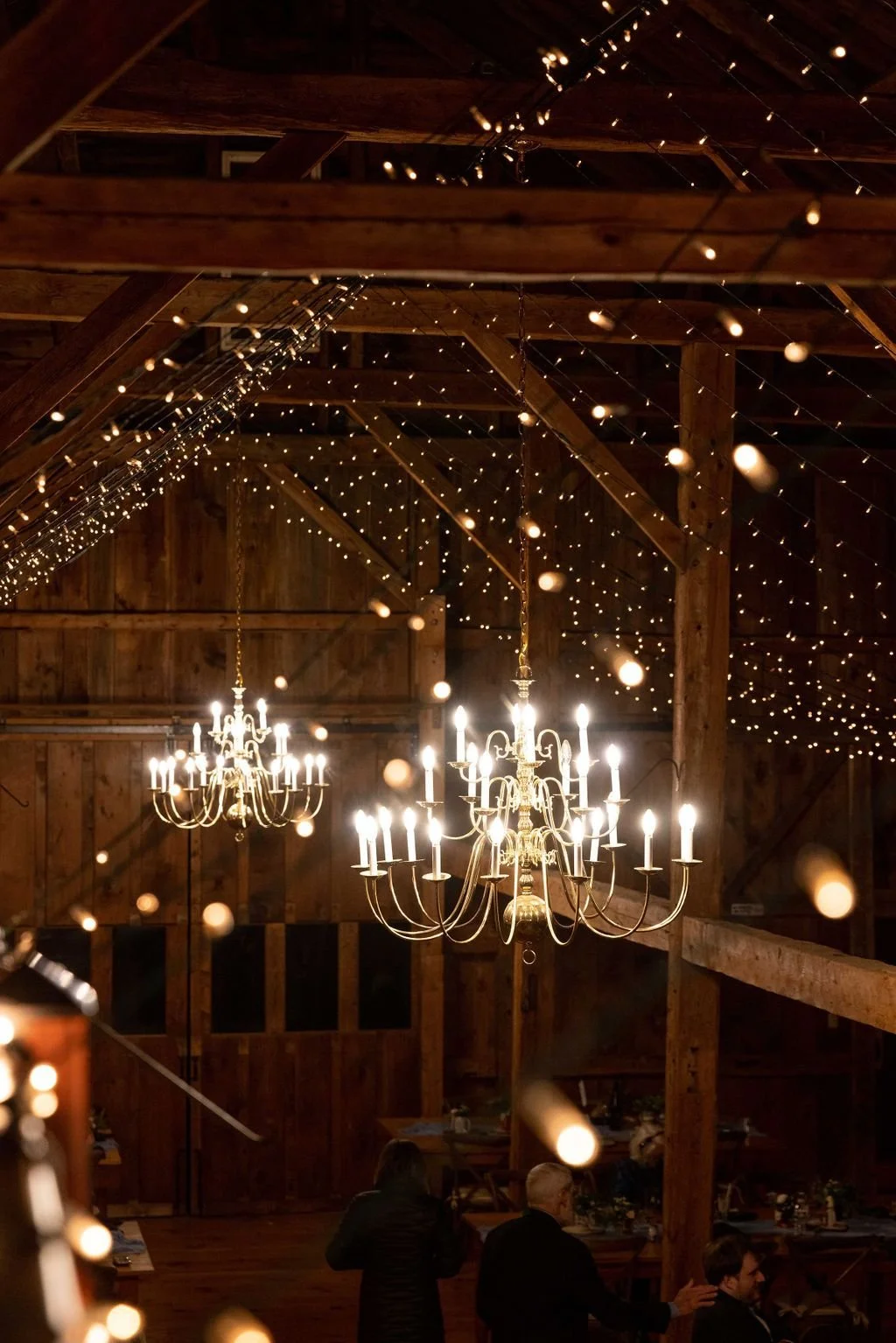 Chandeliers glowing under string lights in the barn at night