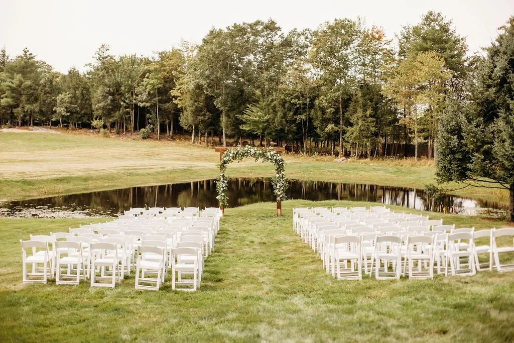 White ceremony chairs facing a floral arch beside the pond