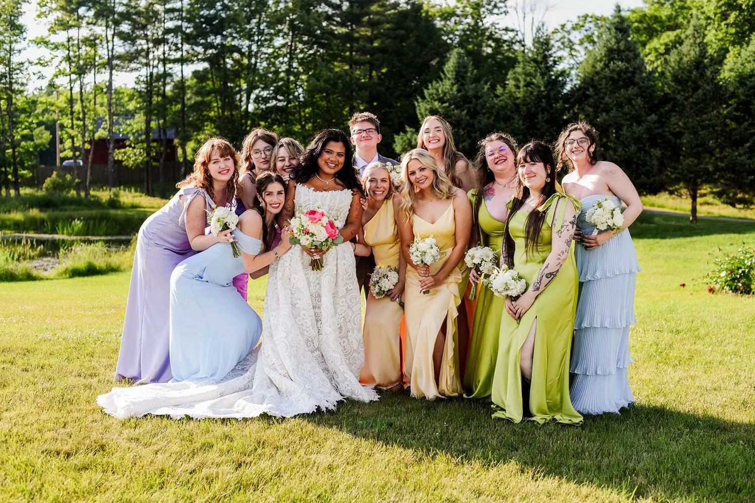 A bride with her bridesmaids in multicolored dresses laughing on the lawn