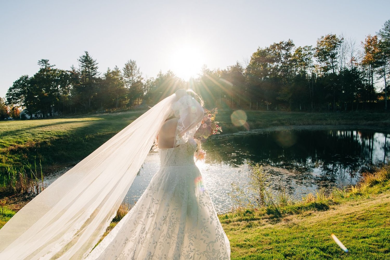 A bride's long veil catching the sunlight beside the pond
