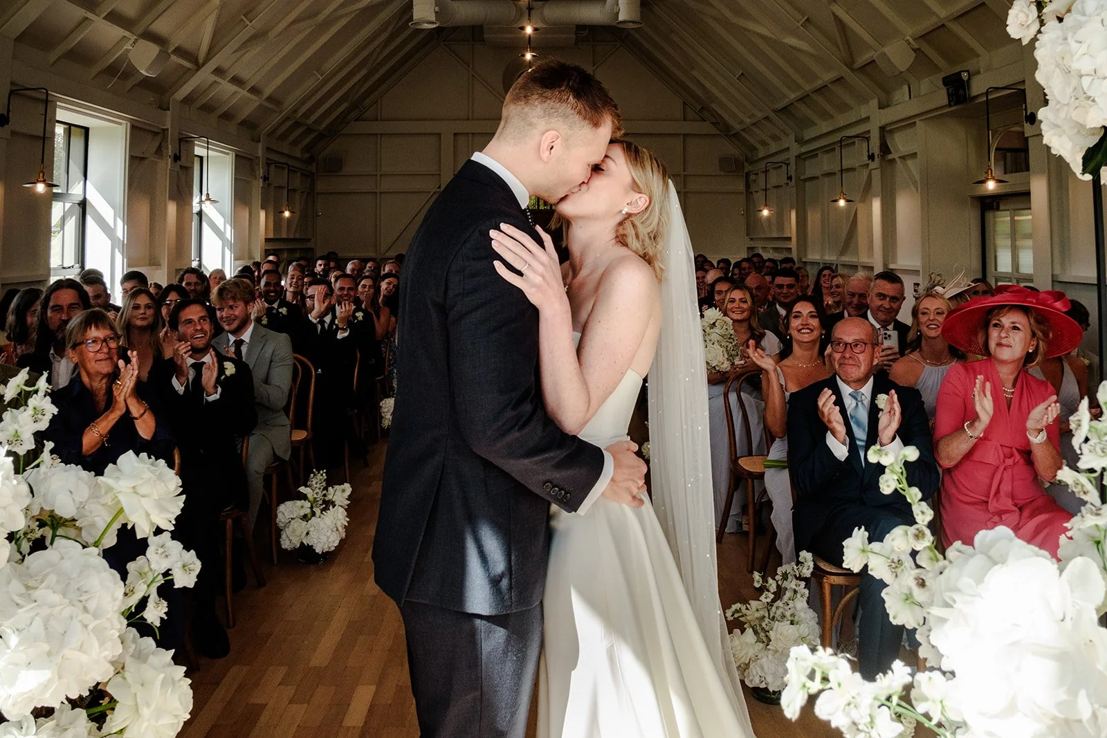 Jack and Abi share their first kiss as husband and wife at Limekiln East Sussex, surrounded by cheering guests and white floral arrangements
